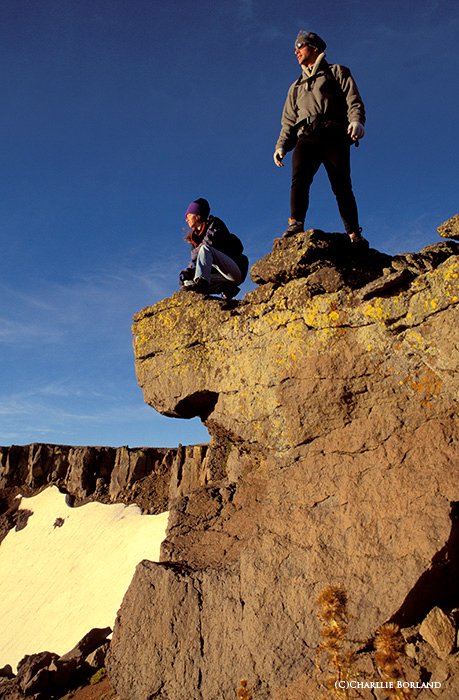 два альпиниста стоят у обрыва на скале, глядя на долину и простор голубого неба