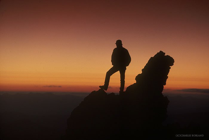 силуэт туриста на вершине скалы, смотрящего на закат на горизонте - советы по приключенческой фотографии