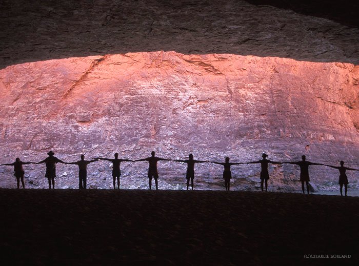 силуэт цепочки людей, держащихся за руки перед скалой, освещенной солнцем пурпурным и оранжевым цветом