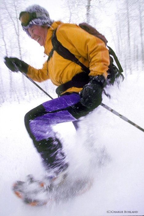 лыжник в желтой куртке и синих штанах, спускающийся по снежному склону
