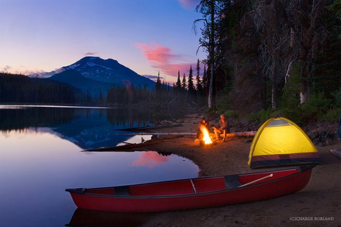 туристы с костром, желтая палатка, красная лодка на берегу озера, гора на горизонте в пурпурно-оранжевом закате
