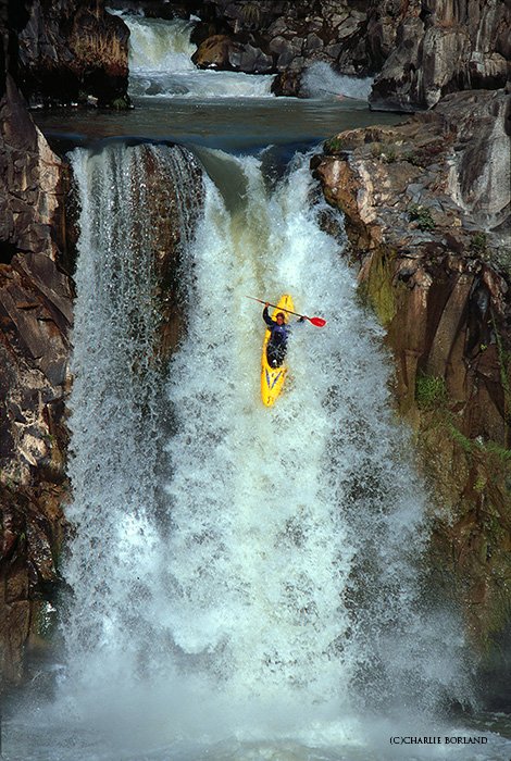 человек гребет по порогам в желтом каноэ, спускаясь по водопаду