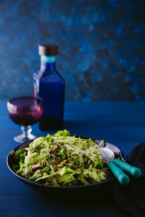 красивый фуд-фотопортрет салата из брокколи, бальзамического уксуса и бокала на синем фоне