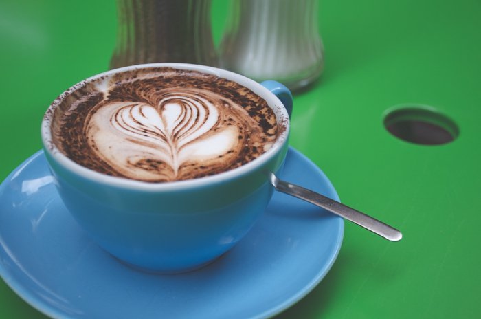 Фото капучино в синей кофейной чашке на зеленом фоне крупным планом демонстрирует цветовой контраст изображений
