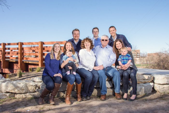 Семейная групповая фотография на улице в яркий день, семья в джинсах и ботинках, деревянный мост и голубое небо за ними
