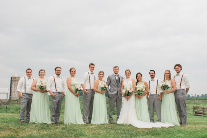Свадебная свита позирует в травянистом поле, подружки невесты в мятных платьях, женихи в подтяжках