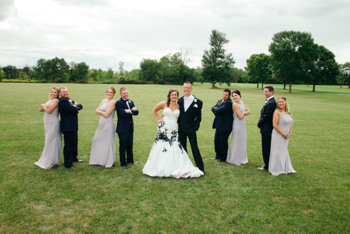 Свадебная свита в широком травянистом поле, каждая пара стоит спина к спине, невеста в белом свадебном платье с замысловатой черной вышивкой