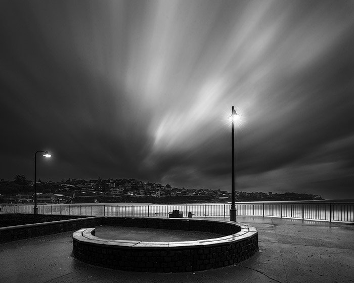 черно-белая фотография с длинной выдержкой на берегу моря, освещенного фонарями ночью