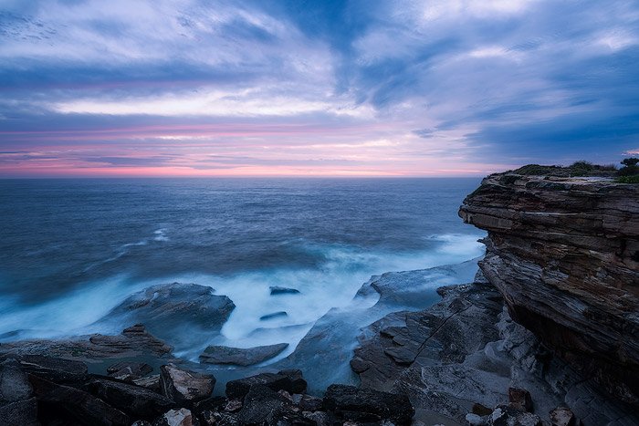 морской пейзаж на вершине скалы. скалистый утес с видом на синее море и пенистые волны, облачное небо и пурпурно-розовый рассвет на горизонте