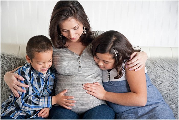 Красивый снимок материнства, на котором двое детей, мальчик и девочка, смотрят и трогают живот беременной мамы