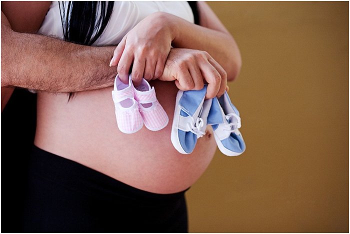крупный план пары, обнимающей беременный живот, держащей розовые и голубые детские туфли