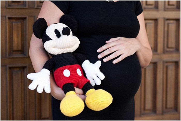 крупным планом беременная женщина держится за живот, рядом с ней мягкая игрушка Микки Маус