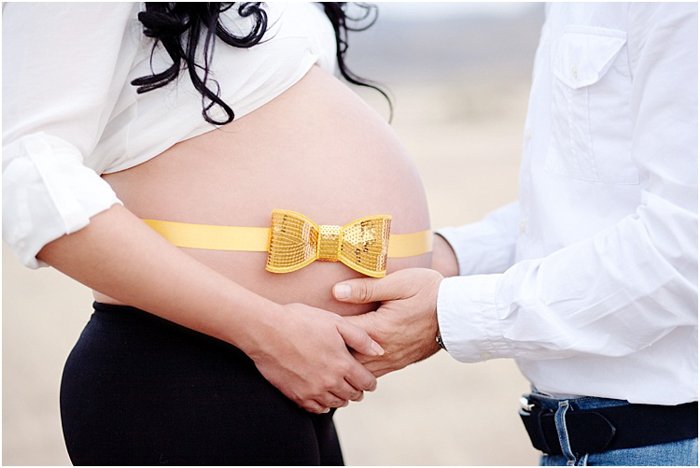 Крупный план мужчины, держащего в руках живот беременной жены, ярко-желтая и золотая лента на ее животе
