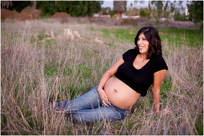 беременная женщина в джинсах и черной рубашке, сидящая в поле