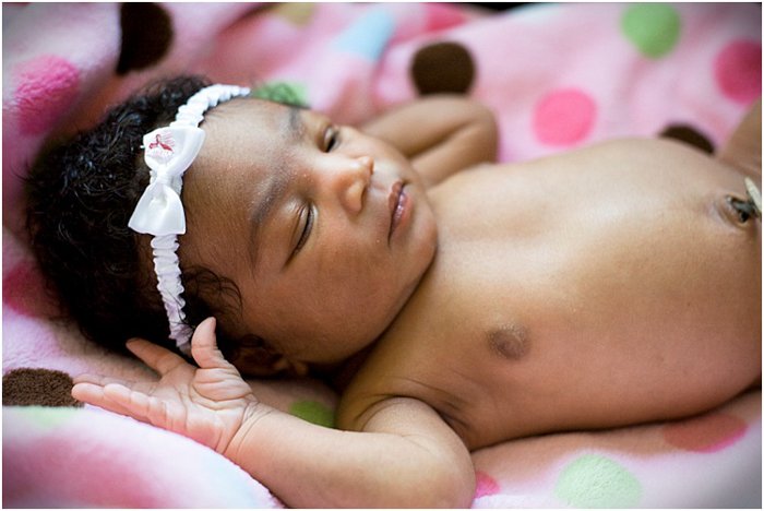 close up of newborn baby girl wearing the white headband sleeping on the pink blanket