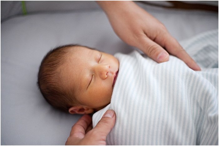 close up of baby wrapped up and sleeping, with parents's hands on him during a newborn portrait session