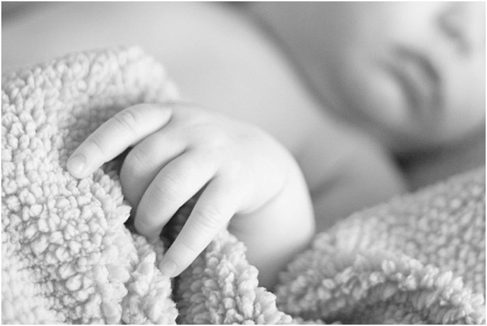 черно-белая фотография руки ребенка, сжимающей одеяло, во время портретной съемки новорожденного