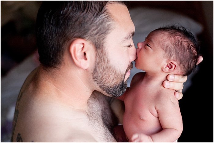 крупный план отца, обнимающего ребенка, ребенок кусает отца за нос во время фотосессии новорожденных