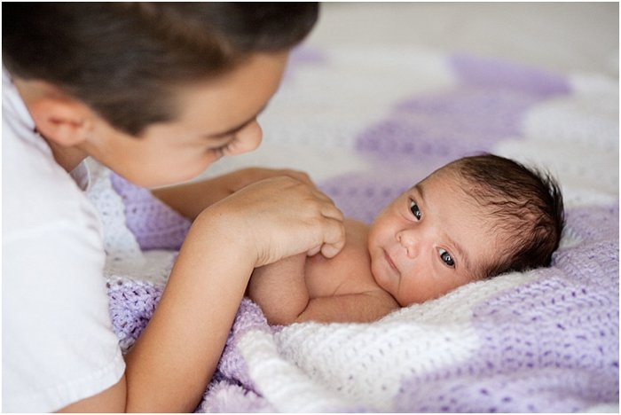 close up старший брат держит за руки новорожденного ребенка во время портретной съемки новорожденных