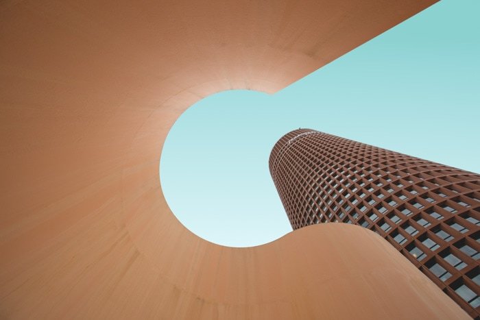Крутая архитектурная фотография, смотрящая вверх через скульптурный элемент рядом с высоким многооконным зданием