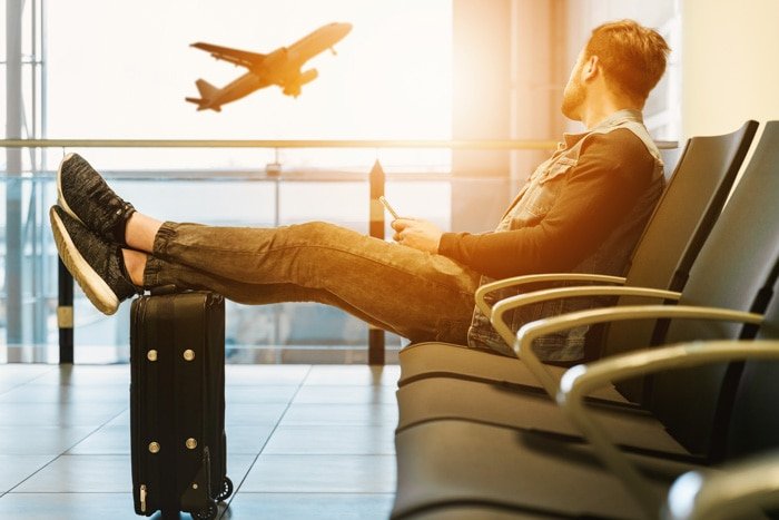 Мужчина сидит в зале ожидания аэропорта, наблюдая из окна за поднимающимся самолетом