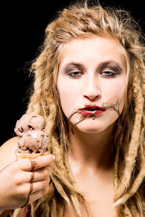Блондинка с шоколадным мороженым на лице на черном фоне - фото реквизит