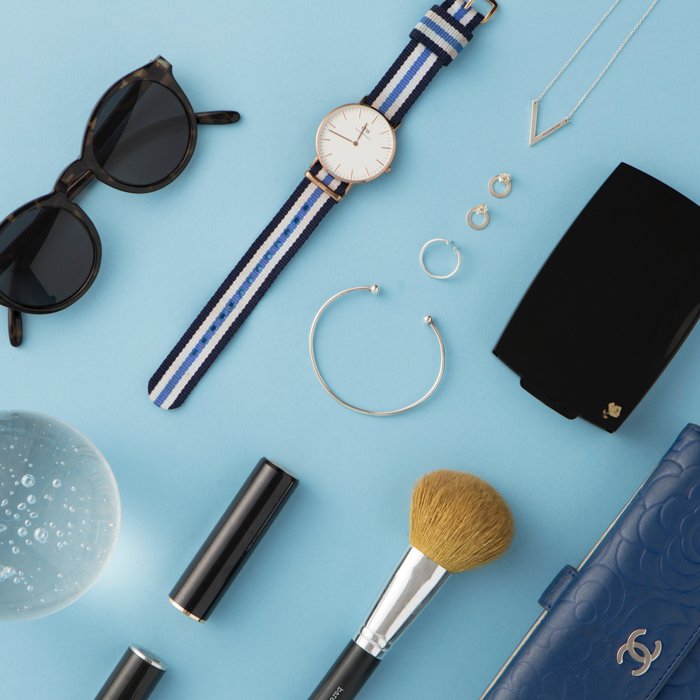 плоский план женских аксессуаров на светло-голубом фоне: часы, серьги, солнцезащитные очки, кисть, кошелек