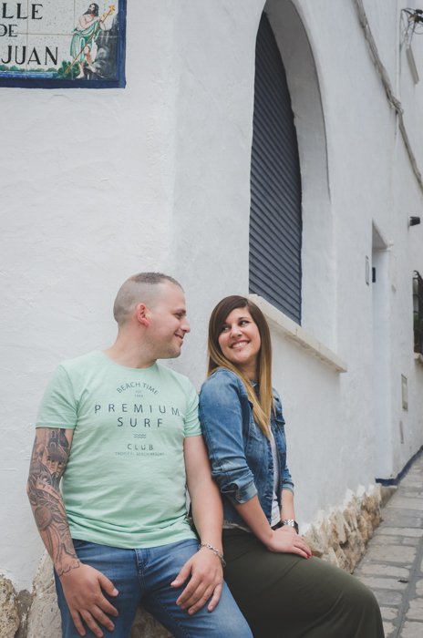 мужчина и женщина сидят на углу белого здания, любовно улыбаясь друг другу