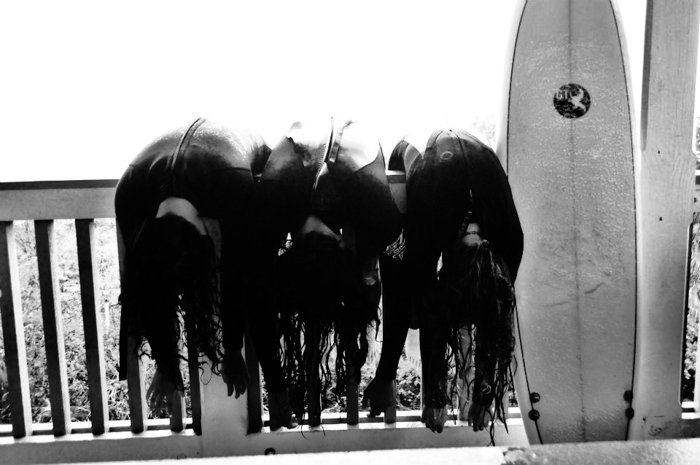 черно-белое фото трех серферов, склонившихся над забором, доска для серфинга, прислоненная к забору - стили фотографии для смартфонов