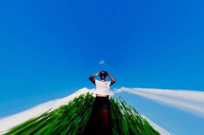 sbstract photo of the man in white shirt posing in front of dark green trees and bright blue sky