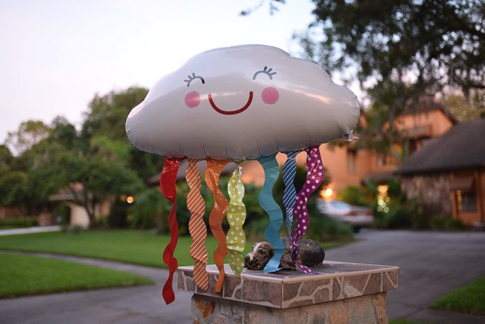 воздушный шар в форме облака с разноцветными серпантинами и улыбкой, парящий в жилом квартале