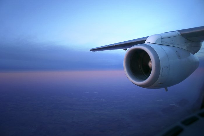 Вид из иллюминатора самолета на крыло и двигатель на фоне синих, фиолетовых и оранжевых сумерек