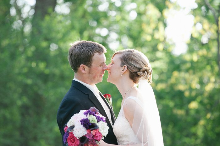Улыбающиеся жених и невеста на фоне зеленых листьев собираются поцеловаться - лучшие советы по редактированию свадебных фотографий