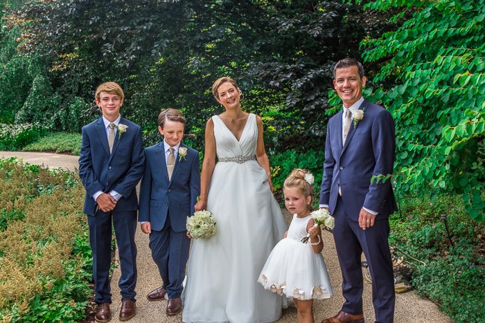 свадебная семья, невеста, жених и трое детей, стоящие на дорожке с кустами и деревьями позади них, HDR монтаж свадебной фотографии