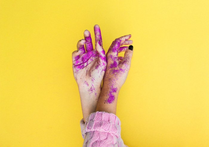 Забавное изображение рук, покрытых краской и блестками, с сильным использованием дополнительных цветов - желтого и фиолетового