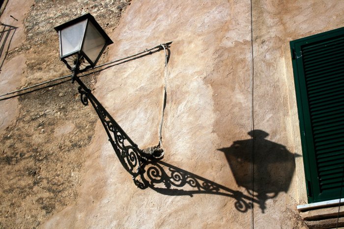 Уличная фотография фонаря с тенью, отбрасываемой на каменную стену