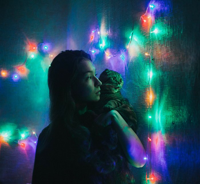 Ночной портрет девушки, держащей кошку в окружении разноцветных рождественских огней