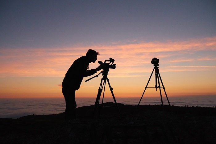 Силуэт фотографа, снимающего зеркальной камерой на штативе на закате