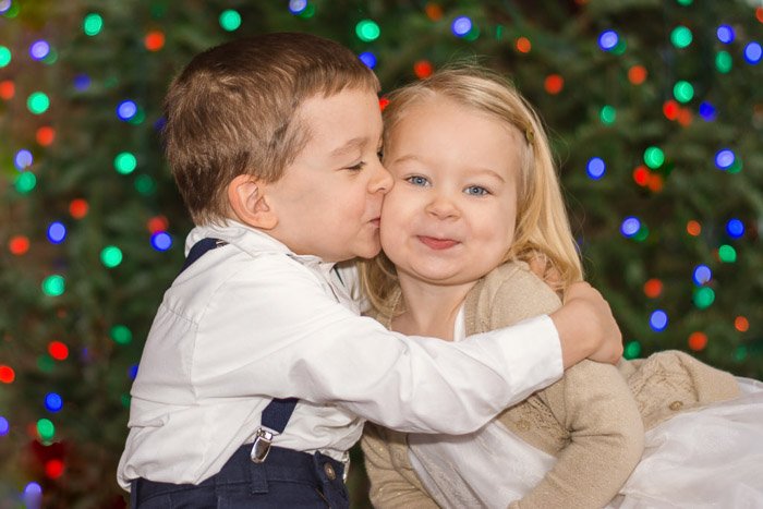 Двое маленьких детей обнимаются на размытом фоне рождественских огней