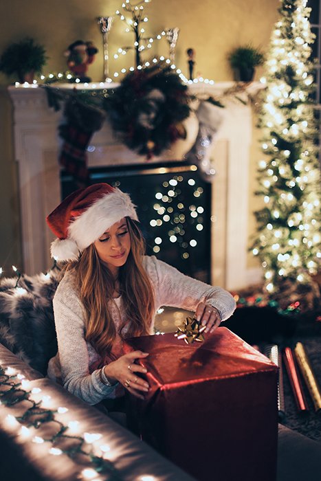 Рождественская фотография женщины, упаковывающей подарки на диване у елки