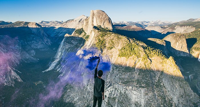 Впечатляющий портрет мужчины, размахивающего синими дымовыми гранатами в горном пейзаже