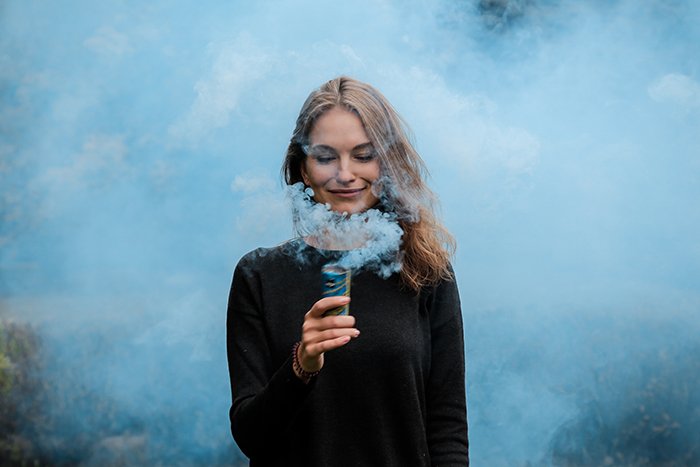 Творческий портрет женщины, держащей возле лица дымовую гранату светло-синего цвета