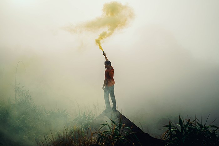 Атмосферный портрет мужчины, размахивающего дымовыми гранатами в пейзажной обстановке