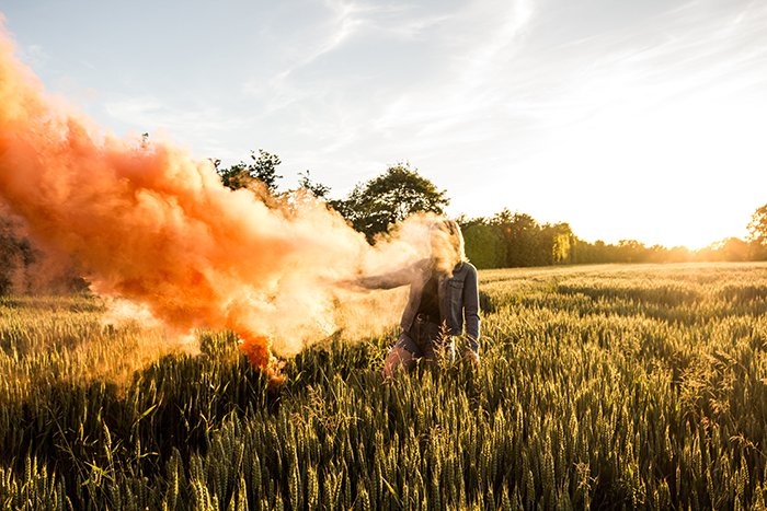Портрет женщины с оранжевыми дымовыми гранатами на кукурузном поле