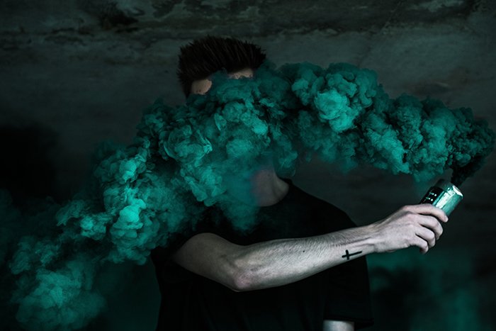 Креативный фотопортрет дымовой шашки мужчины, держащего зеленую дымовую гранату возле лица