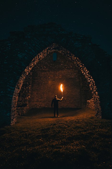 Драматический и загадочный портрет человека, держащего пламя под аркой ночью - советы по пожарной фотографии