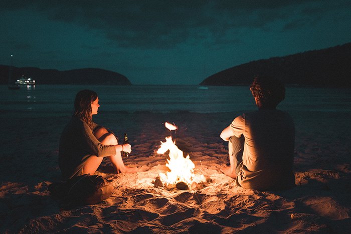 Пара сидит у костра на пляже ночью - фотографии костра