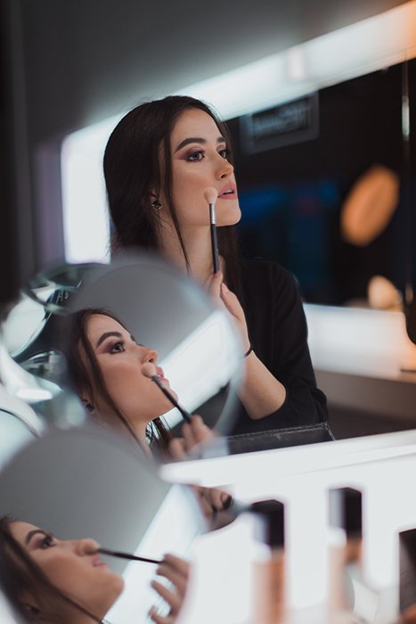 Диптих портрет брюнетки-модели, отражающейся в нескольких зеркалах во время нанесения макияжа