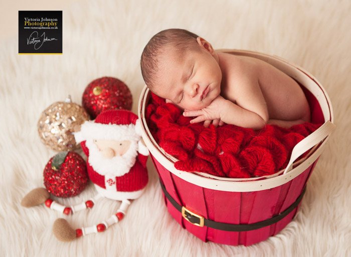 Новорожденный в красной корзине в окружении рождественского реквизита для фотографии новорожденных