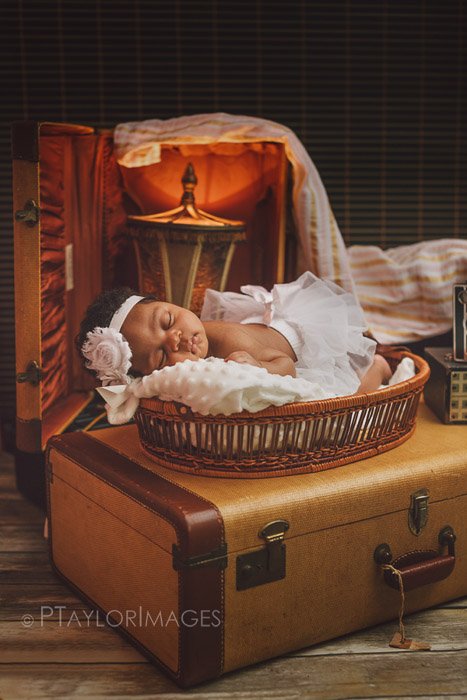 новорожденный позирует на чемодане среди других реквизитов для фотосъемки новорожденных